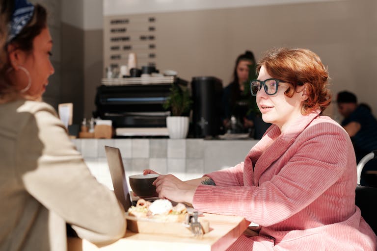 Two women conversing over coffee and snacks in a bright, welcoming café environment.