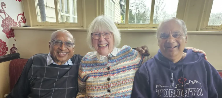 Three people sitting on a couch, smiling and hugging.