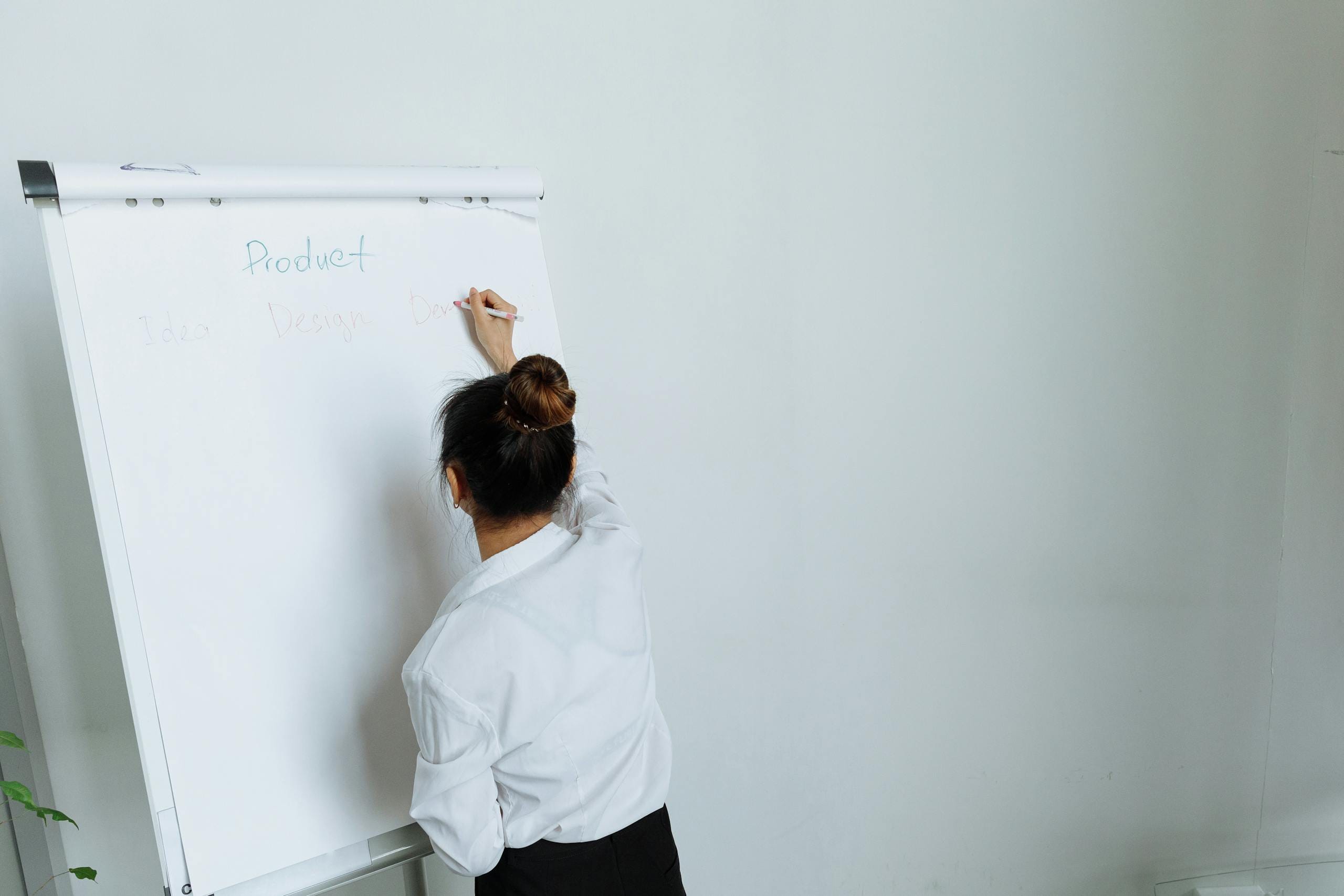 A woman in a white shirt writes on a flipchart during a presentation in an office.